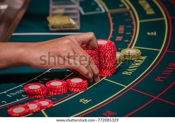 A Hand of Dealer Organizing the Red & Green Baccarat Chips on Baccarat Gaming table.